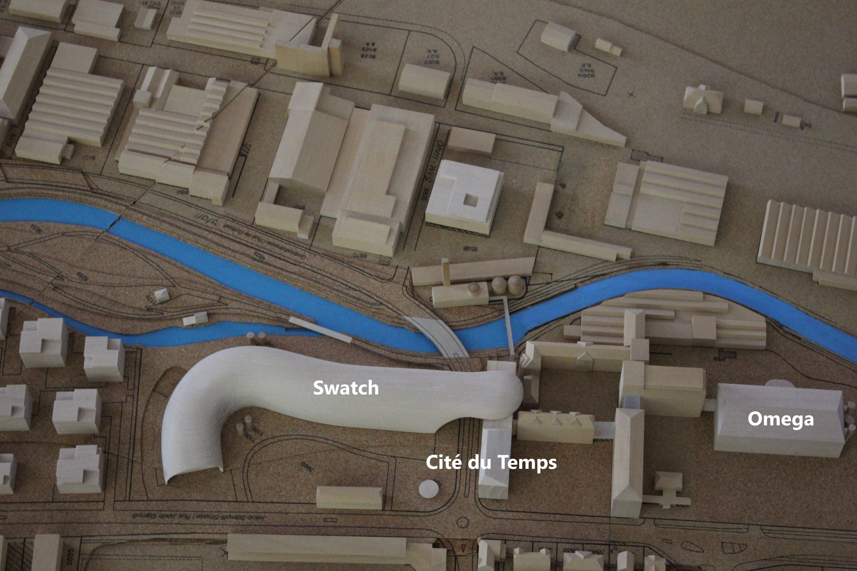 Ein Miniaturmodell einer Stadtlandschaft mit einem Fluss, Gebäuden, Straßen und Text.