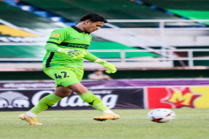 Ein Mann in einem grünen Torwarttrikot schießt einen Fußball auf einem Rasenfeld in einem Stadion, im Hintergrund sind Banner mit der Aufschrift "Chivas USA vs Mexico City, 3:1, Copa Libertadores".