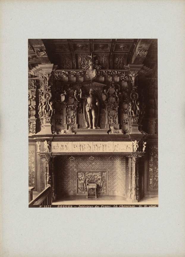 Altes Schwarz-Weiß-Foto eines Kamins mit einer zentralen Statue, umgeben von Wandskulpturen und einer dekorierten Decke, mit Text unten.