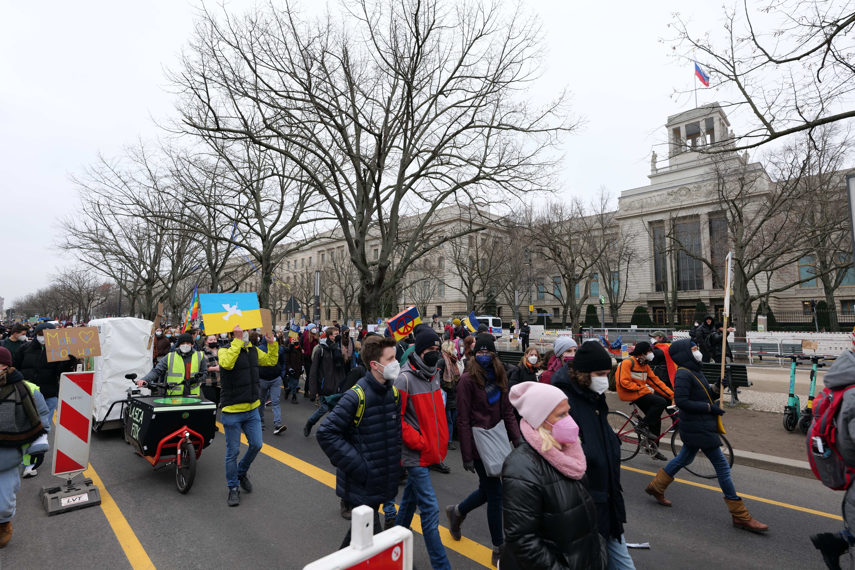 Eine große Protestdemo in Washington, D.C. am 21. Januar 2020, mit Menschen, die marschieren, Schilder halten und Fahrräder fahren, vor einem Gebäude auf einer Straße unter einem klaren blauen Himmel.