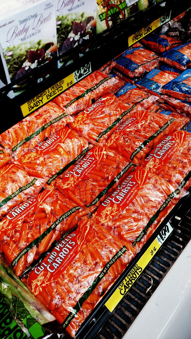 Ein Supermarkttisch mit verschiedenen verpackten Lebensmitteln, darunter Gemüsepackungen, jeweils mit angehängten Preisschildern.