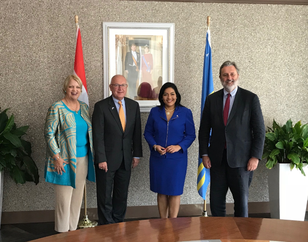 Eine Gruppe strahlender Menschen, die um einen Tisch mit Papieren stehen, umgeben von Fahnen, Topfpflanzen und einem Foto auf dem Wandregal, feiert die Unterzeichnung eines Memorandums zwischen den Vereinigten Staaten und Kanada.