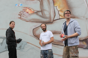 Menschen stehen und halten Farbsprühflaschen vor einer Wand mit Graffiti.