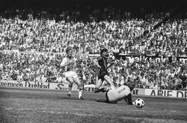 Schwarzes und weißes Foto von Männern, die auf einem Feld Fußball spielen, mit Zuschauern im Hintergrund und einem Bundesliga-Banner mit der Aufschrift "Bundesliga 1978-79 Ajax 1-1 Hannover 96".