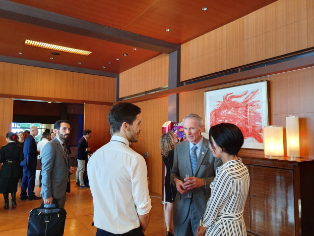 Menschen, die in einem Raum mit einer hölzernen Wand mit einem Foto Rahmen und Beleuchtung stehen und sprechen, einige halten Taschen auf einer Kunstausstellung im Nationalmuseum Singapur.