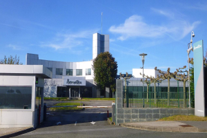 Ein großes Gebäude mit zahlreichen Fenstern und einem Tor davor, umgeben von Straßenlaternen, Lampen, Gittern, Bäumen, Gras und einem bewölkten Himmel im Hintergrund, das als Hauptsitz von Iberostica in den Niederlanden dient.