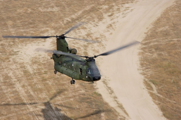 Militärhelikopter über einer Schotterstraße mit sichtbarem Boden darunter.