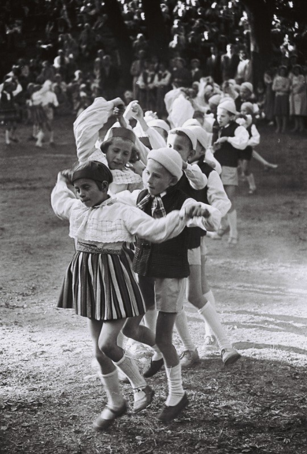 Schwarz-weiß-Foto von Kindern, die in einem Park tanzen, mit ein paar Zuschauern im Hintergrund und ein paar Bäumen im Bild.
