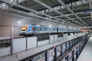 Ein blauer und weißer Zug fährt durch ein großes Gebäude mit einer Plattform auf der rechten Seite und einer Decke mit Stäben und Lichtern überhaupt, Teil eines neuen Zugsystems in Deutschland.