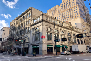 Ein großes Eckgebäude, ehemals ein Starbucks, umgeben von anderen Gebäuden, Straßenlaternen, Verkehrszeichen, Kraftfahrzeugen, Fußgängern, Bäumen und einem bewölkten Himmel in Chicago.