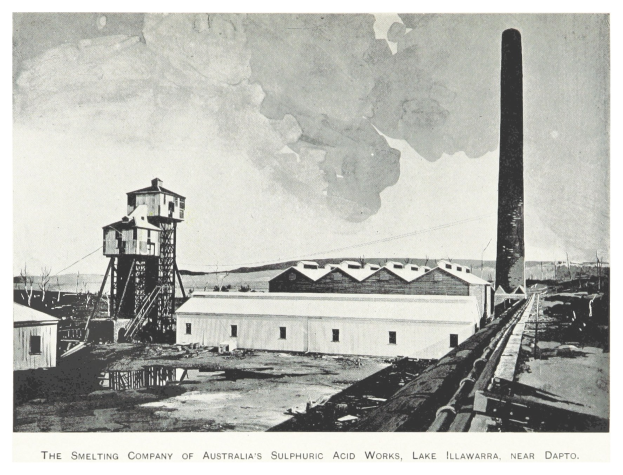 Schwarzes und weißes Foto einer Fabrik mit mehreren Gebäuden, einem hohen Turm und Rauch, der aus einem Schornstein aufsteigt, mit Text am unteren Rand.