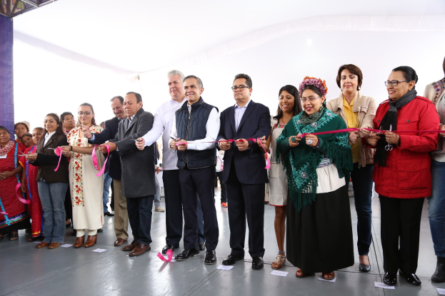 Eine Gruppe von Menschen, die eine Schnur schneiden, mit einer Säule links, verstreuten Papieren auf dem Boden und einem weißen Tuch im Hintergrund.