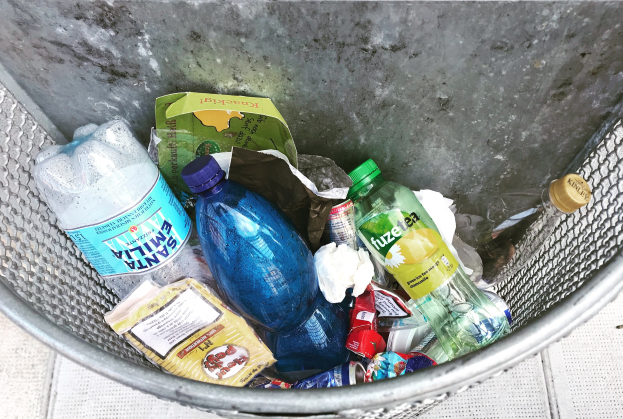 Ein Metallmüllcontainer voller Plastikflaschen, Verpackungen und anderer Gegenstände.
