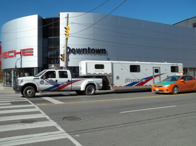 Polizeilaster vor einem Gebäude mit Text geparkt, mit einer Ampel und Kabeln im Vordergrund, Bäumen und einem klaren blauen Himmel im Hintergrund.