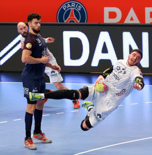 Eine Gruppe von M"annern, die auf einem Platz Handball spielen, wobei einer den Ball h"alt, und ein Paris Saint-Germain-Futsal-Siegesschild im Hintergrund.