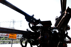 Eine Maschine ist im Vordergrund mit elektrischen Masten, Kabeln, Barrieren, Pflanzen und Himmel im Hintergrund.