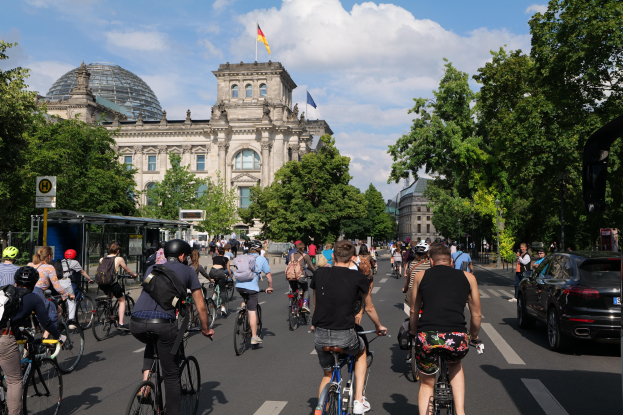 Eine Gruppe von Menschen, die auf Fahrrädern eine von Bäumen gesäumte Straße in Berlin, Deutschland, entlangfahren.