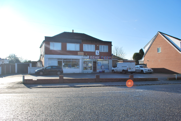 Gewerbliches Grundstück zum Verkauf an der St Johns Road, Luton, Bedfordshire, mit Gebäuden, Fahrzeugen, einer Wand, Bäumen und einem bewölkten Himmel.