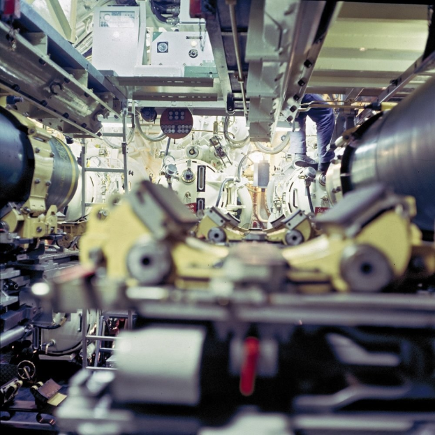 Ein Mann steht auf einer Maschine in einem industriellen Raum und arbeitet daran zwischen anderen Maschinen.