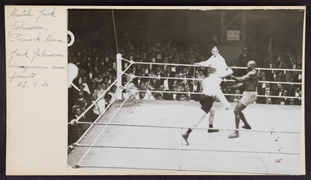 Schwarzes und weißes Foto von zwei Boxern im Ring, beschriftet mit 'Jack Johnson vs Frank Morgan', mit Zuschauern dahinter und einer Wand im Hintergrund.