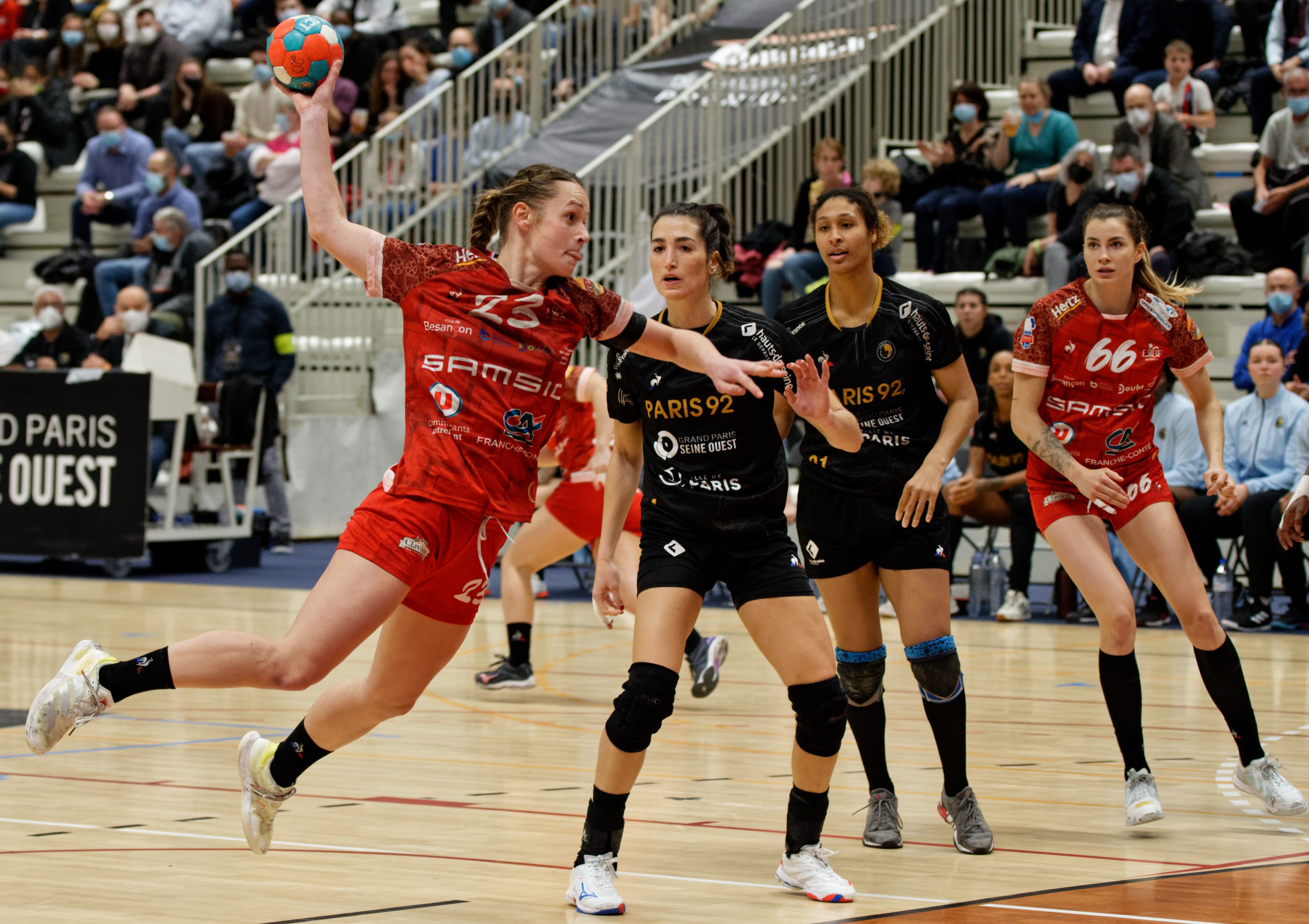 Frauen spielen Handball auf einem Feld während der Handball-Weltmeisterschaft 2019 in Paris, mit Zuschauern im Hintergrund und einer Anzeigetafel, die "Frankreich vs. Frankreich" anzeigt.