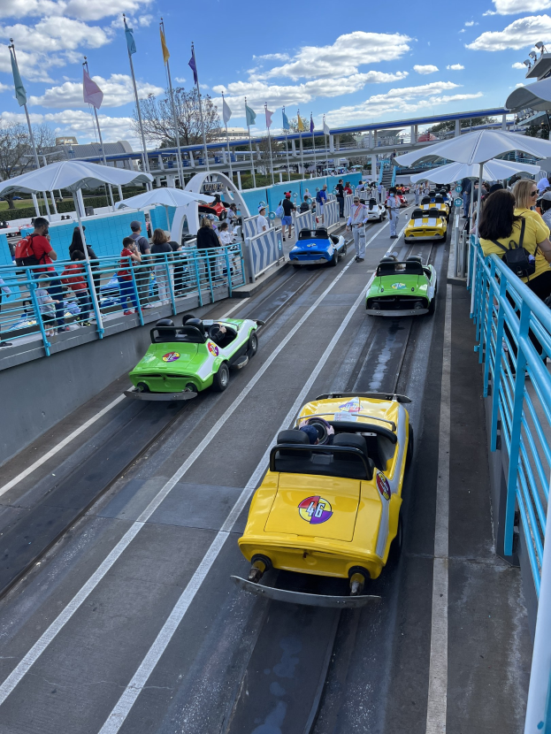 Menschen, die eine Achterbahn in Disney's Hollywood Studios fahren, umgeben von Geländern und Fahnen, mit Bäumen und Gebäuden im Hintergrund unter einem bewölkten Himmel.