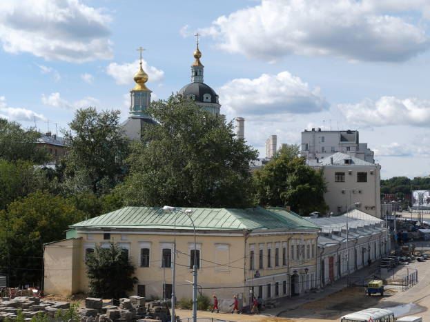 Eine Stadtansicht mit der Kirche der Versöhnung am Nerl im Hintergrund, umgeben von Gebäuden, Bäumen, Straßeninfrastruktur, Fahrzeugen, Fußgängern und einer bewölkten Himmel.