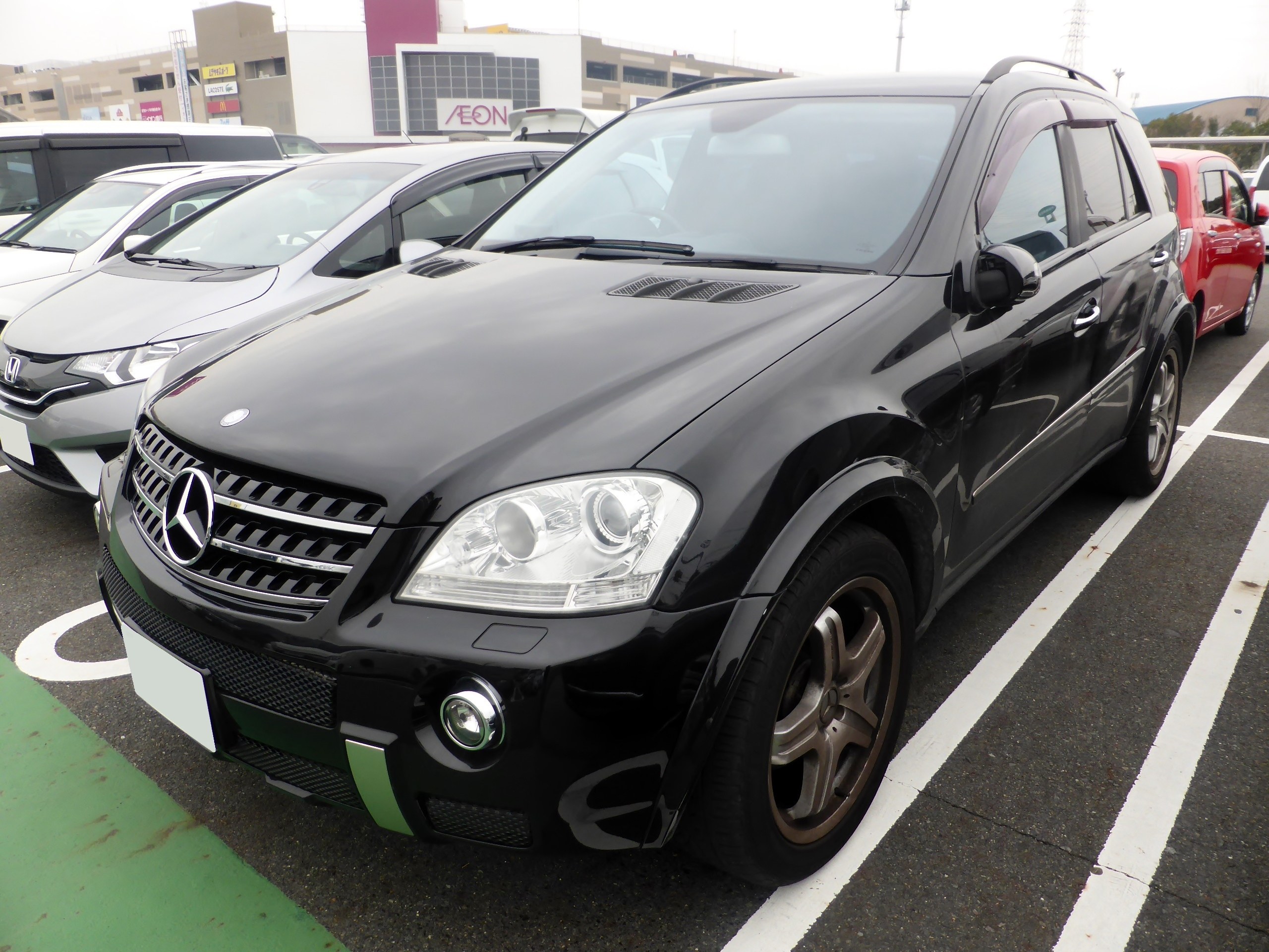 Schwarzer Mercedes-Benz ML 350 CDI Blueefficiency auf einem Parkplatz mit Gebäuden, Masten, Bäumen und einem klaren blauen Himmel im Hintergrund geparkt.