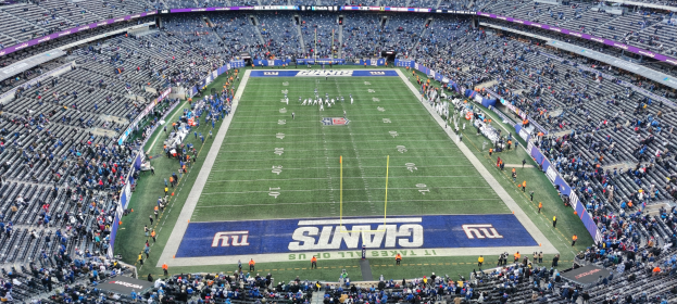Ein volles Fußballstadion mit Spielern auf dem Feld, Torpfosten und Texttafeln, aus einer erhöhten Perspektive betrachtet.
