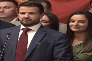 Ein Mann im Anzug spricht in ein Mikrofon an einem Rednerpult, mit einem Banner dahinter und einer Menge davor, wahrscheinlich zu einem Verbot der sozialen Medien durch die Regierung.