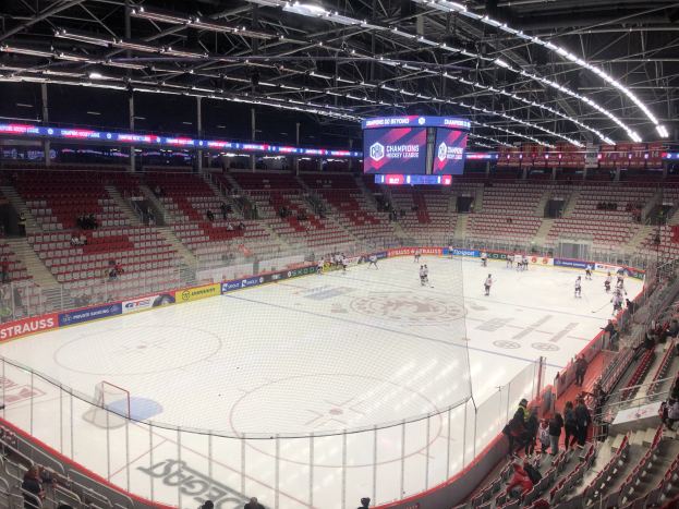 Eishockeyspiel in einer großen Arena mit Zuschauern, ein von einem Zaun umgebenes Spielfeld, ein Display mit "St. Louis Blues vs Detroit Red Wings", Metallrahmen, Deckenbeleuchtung und Dach.