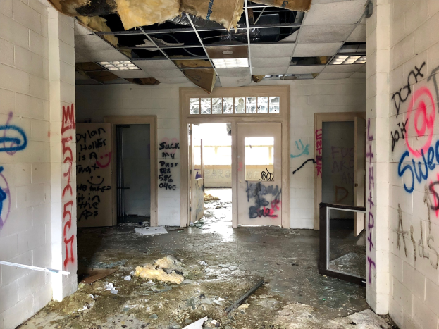 Verlassenes Gebäude mit graffiti-versehenen Wänden und Decke, Schutt auf dem Boden, mehreren Türen und Fenstern im Hintergrund und verstreuten Gegenständen.