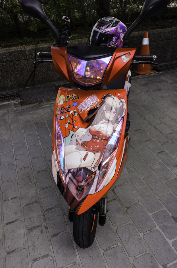 Ein oranges E-Scooter auf dem Seitenstreifen mit einem Helm darauf, mit einem Verkehrskegel, einer Wand und Bäumen im Hintergrund.