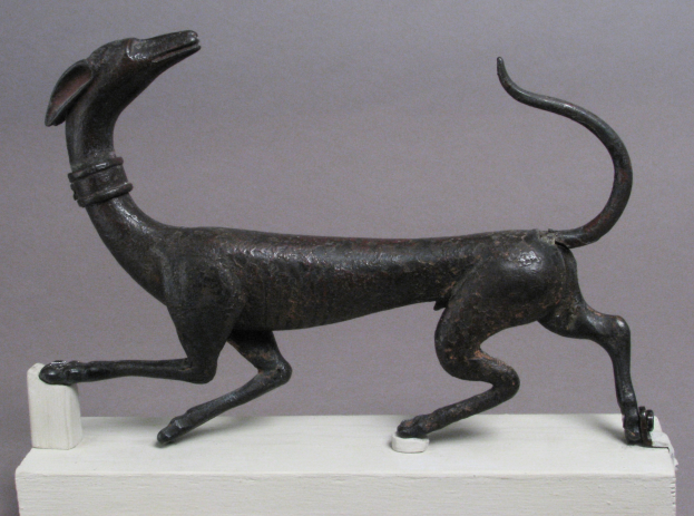 Eine Bronzestatuette eines Greyhounds auf einem weißen Sockel vor einem grauen Hintergrund mit detailliertem Fell und Zügen.