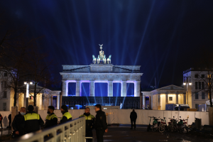 Eine Gruppe von Polizisten vor dem Brandenburger Tor in Berlin, Deutschland, mit einem Geländer, parkenden Fahrrädern, Gebäuden, Bäumen, Laternenmasten und einer Statue auf einem Gebäude im Hintergrund, unter einem sichtbaren Himmel.
