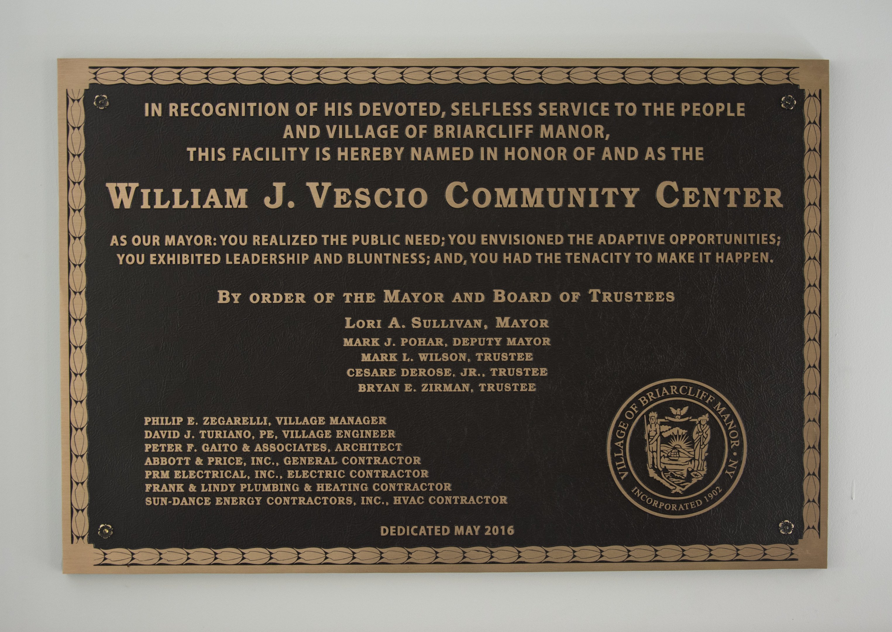 Schwarzes rechteckiges Schild an einer Gebäudewand mit der zentrierten weißen Schrift "William J. Vesco Community Center" in fetter Schrift.