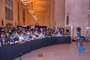 Ein Konzertbild mit einer Menschenmenge, einem Mann, der auf der rechten Seite Gitarre spielt und singt, einer Wand und Fenstern im Hintergrund, Lichtern oben und einem Boden unten.