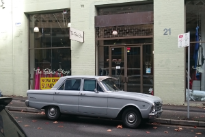 Ein silberner Wagen, der auf einer Straße vor einem Gebäude mit mehreren Türen, einem Pfahl mit einem Schild und Text darauf geparkt ist.