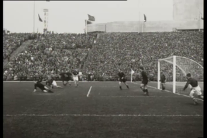 Ein Schwarz-Weiß-Foto eines Fußballspiels im Stadion, mit Spielern auf dem Feld und einem Torpfosten auf der rechten Seite, Zuschauern in den Rängen und Fahnen mit Stangen im Hintergrund. Der Text "1958-1958 WM-Finale - Manchester United v Liverpool" ist oben und unten auf dem Bild zu sehen.