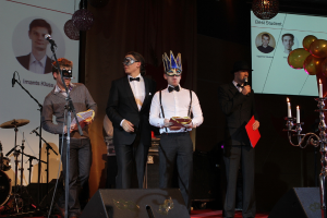 Vier Personen auf einer Bühne, wobei die Person auf der rechten Seite in ein Mikrofon spricht.