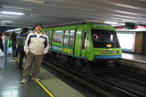 Ein Zug auf einem Bahngleis mit Menschen, die links stehen und ein Dach oben im Bild.