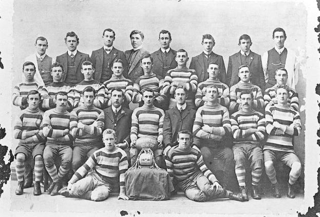Schwarzes und weißes Foto einer Fußballmannschaft mit sitzenden und stehenden Spielern, einem Helm in der Mitte und einem unscharfen Hintergrund.