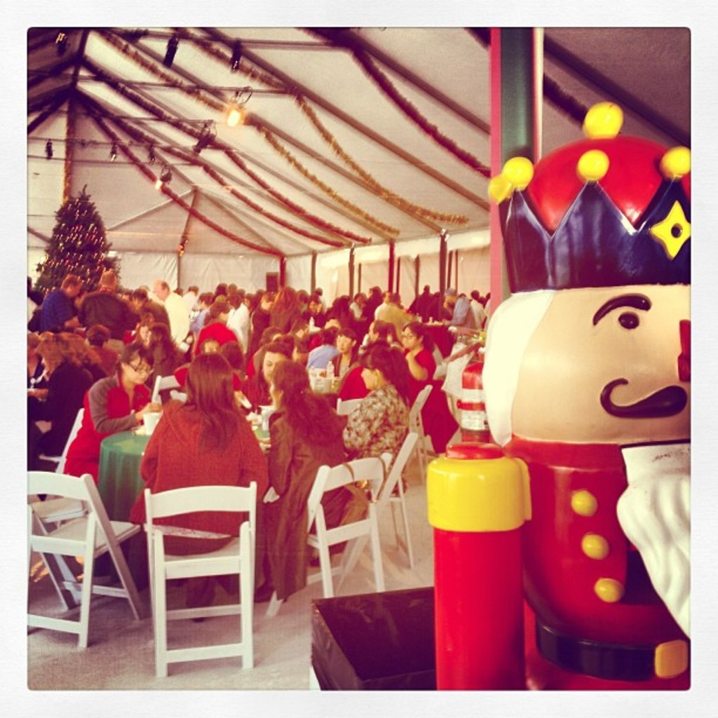 Eine Gruppe von Menschen feiert Weihnachten in einer Hütte, mit einem geschmückten Baum, weißen Stühlen, einem roten Spielzeug-Sicherheitsmann und einer schwarzen Krone.