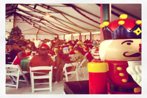 Eine Gruppe von Menschen feiert Weihnachten in einer Hütte, mit einem geschmückten Baum, weißen Stühlen, einem roten Spielzeug-Sicherheitsmann und einer schwarzen Krone.