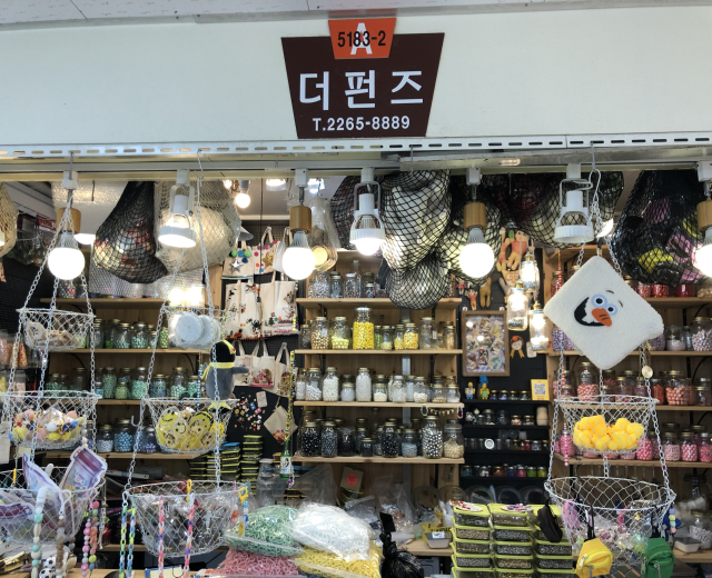Ein unordentlicher Laden mit verschiedenen Gegenständen wie Körpchen, Lichtern, Flaschen und Spielzeugen, die auf Gestellen ausgestellt sind, mit einem Schild öber dem Eingang, das ihn als einen der besten koreanischen Läden in Seoul ausweist.