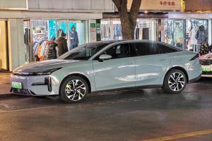 Ein Mitsubishi Lancer EV-Elektroauto, das nachts auf einer Straße geparkt ist, umgeben von Gebäuden, Geschäften, Schaufensterpuppen mit Kleidern, Schildern mit Text, Lichtern und anderen Objekten.