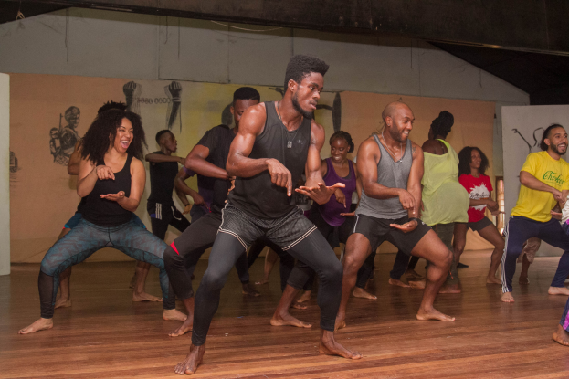 Eine Gruppe von Menschen tanzt in einem Raum mit Gemälden an den Wänden und einer Decke darüber, wahrscheinlich an einem Choreografie-Kurs an der Universität Chicago teilnehmend.
