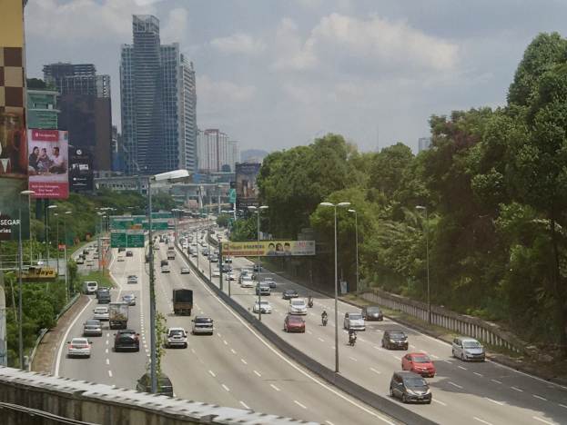 Eine belebte Autobahn mit hohen Gebäuden, Straßeninfrastruktur, Bäumen und einem bewölkten Himmel.