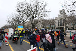 Eine großle Gruppe von Menschen marschiert bei einer Demonstration durch eine Straße in Washington, D.C., mit Schildern und Bannern, einige fahren Fahrräder, unter einem klaren blauen Himmel.