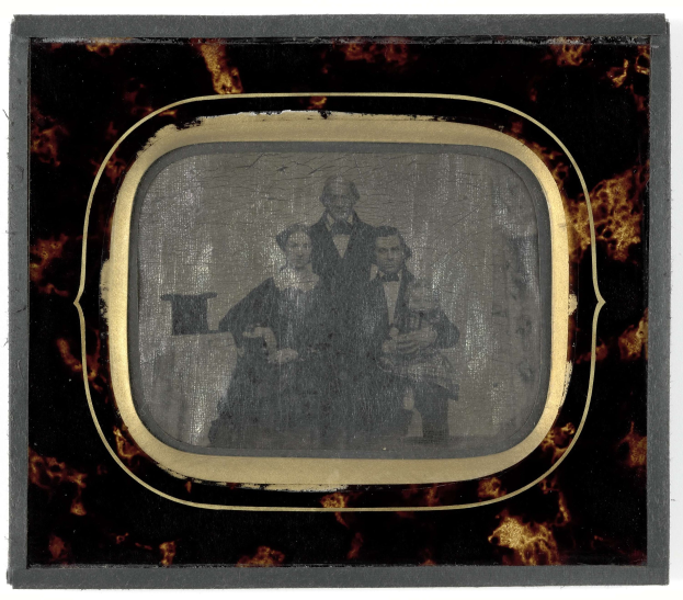 Schwarz-weißes Foto eines Mannes in Anzug und Krawatte und einer Frau in unbekannter Kleidung, die vor einem alten Fernseher stehen und ernst schauen.